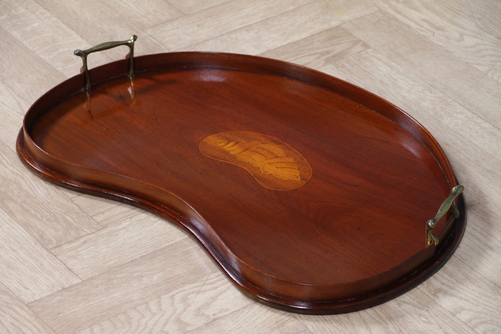 An Edwardian kidney-shaped solid mahogany serving tray featuring a central inlaid shell motif and two brass carrying handles. View XVI