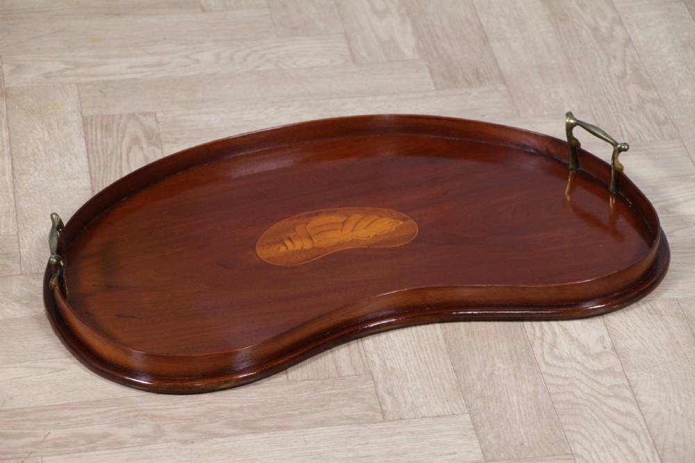 An Edwardian kidney-shaped solid mahogany serving tray featuring a central inlaid shell motif and two brass carrying handles. View XVII