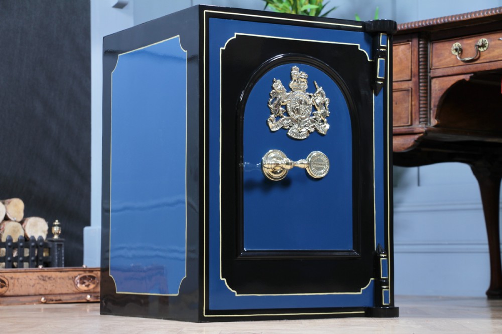 A heavy restored Victorian cast iron safe featuring a deep blue and black lacquered exterior with gold pinstriping and a brass royal coat of arms crest.