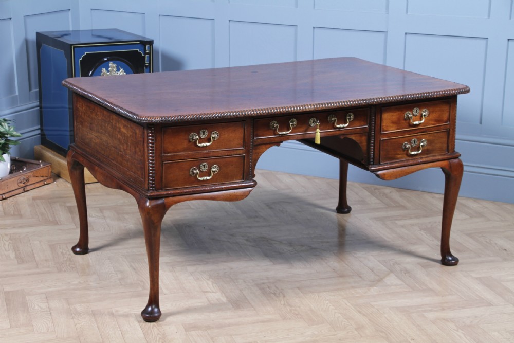 A Georgian mahogany writing desk featuring a rectangular top, central kneehole drawer flanked by side drawers, polished brass handles, and cabriole legs ending in pad feet.