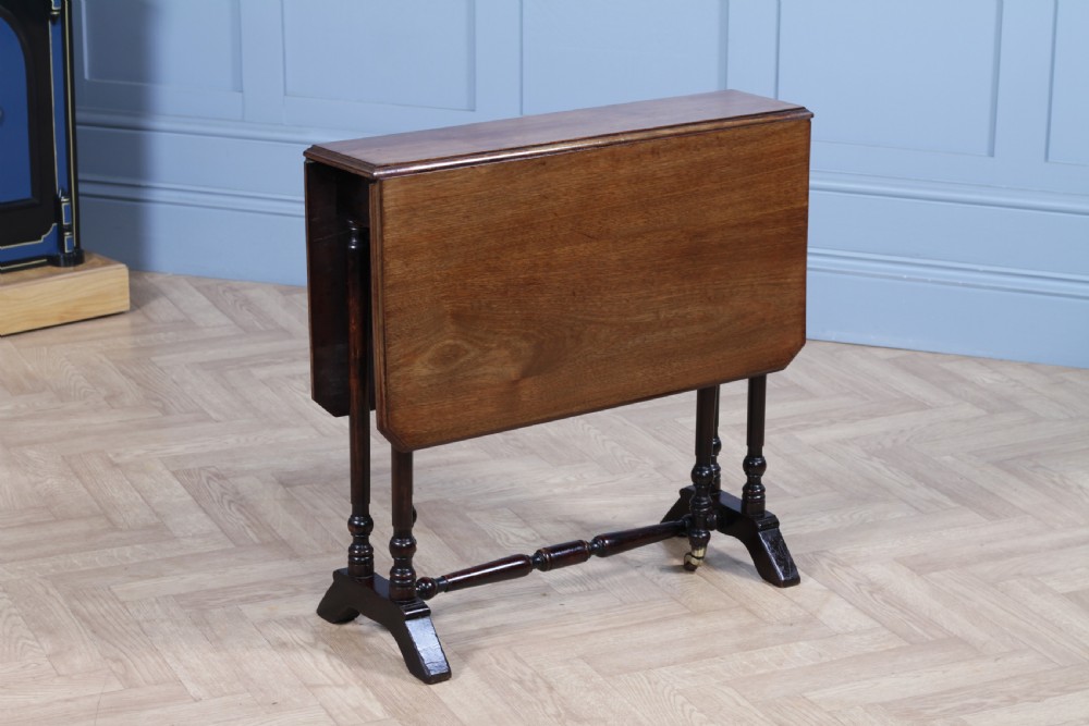 An Edwardian solid mahogany Sutherland table shown folded with turned legs, a lower stretcher bar, and small castors.