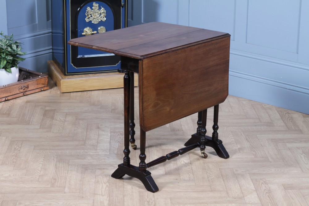 An Edwardian solid mahogany Sutherland table shown folded with turned legs, a lower stretcher bar, and small castors. View II