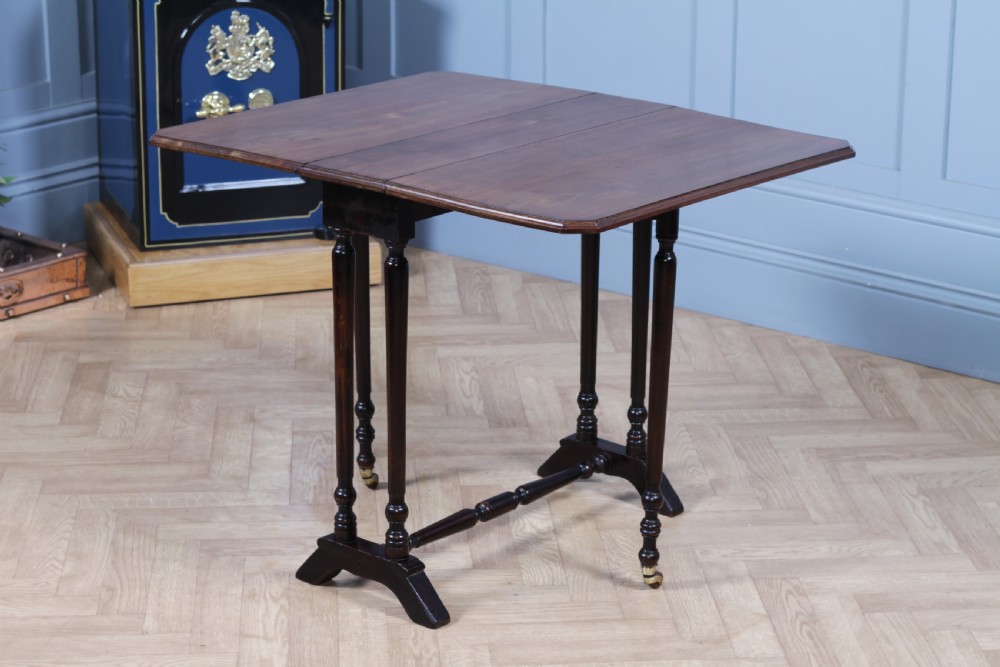 An Edwardian solid mahogany Sutherland table shown folded with turned legs, a lower stretcher bar, and small castors. View III