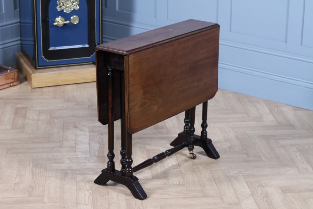 An Edwardian solid mahogany Sutherland table shown folded with turned legs, a lower stretcher bar, and small castors. View V