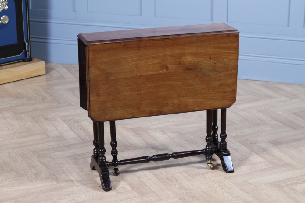 An Edwardian solid mahogany Sutherland table shown folded with turned legs, a lower stretcher bar, and small castors. View VI