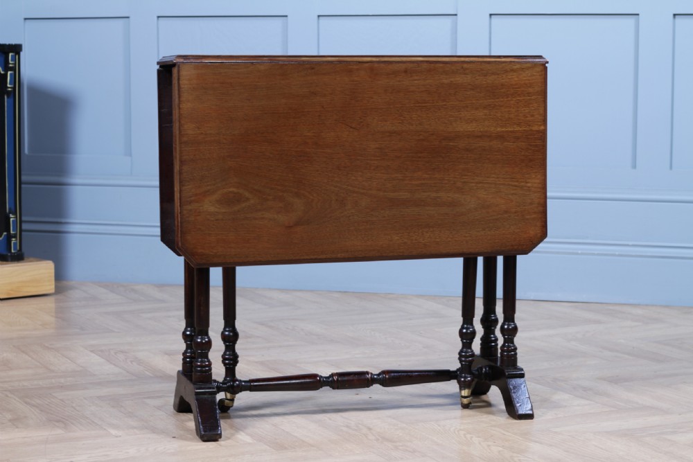 An Edwardian solid mahogany Sutherland table shown folded with turned legs, a lower stretcher bar, and small castors. View VIII
