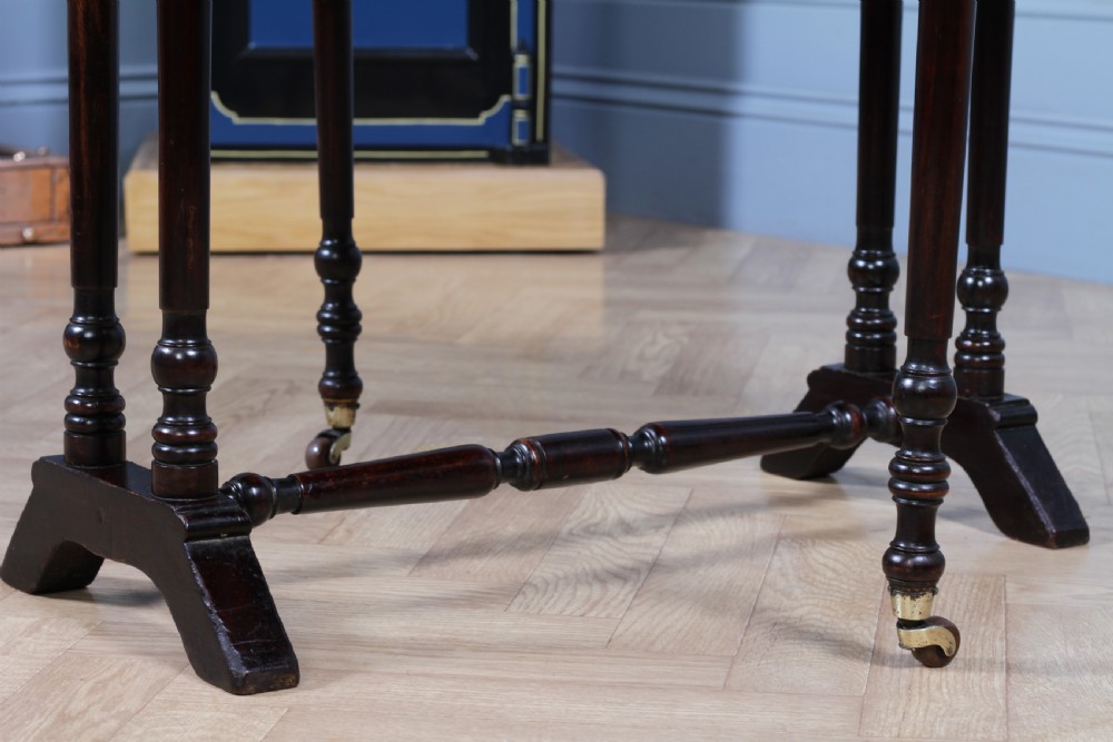 An Edwardian solid mahogany Sutherland table shown folded with turned legs, a lower stretcher bar, and small castors. View X