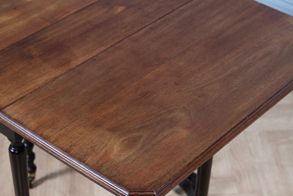 An Edwardian solid mahogany Sutherland table shown folded with turned legs, a lower stretcher bar, and small castors. View XII