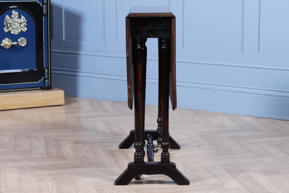 An Edwardian solid mahogany Sutherland table shown folded with turned legs, a lower stretcher bar, and small castors. View XIII
