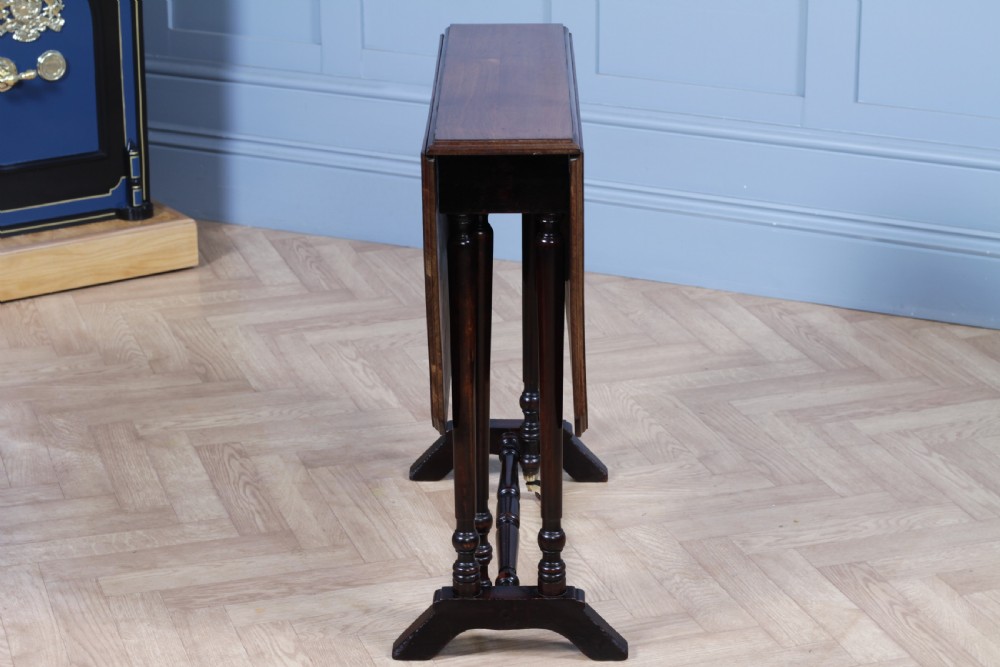 An Edwardian solid mahogany Sutherland table shown folded with turned legs, a lower stretcher bar, and small castors. View XIV