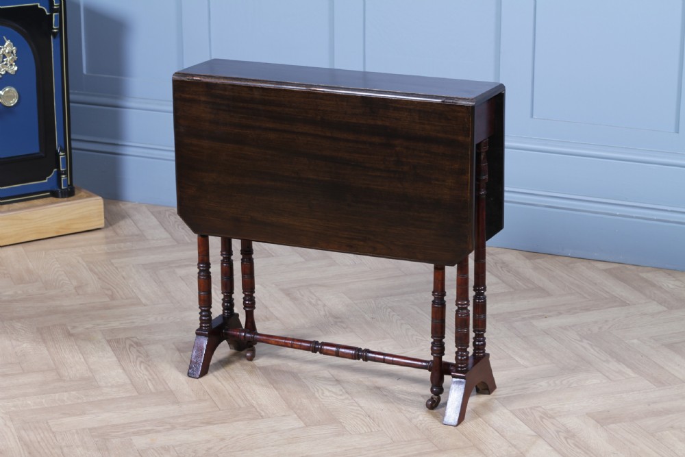 An Edwardian solid mahogany Sutherland table with folded drop-leaf sides, turned spindle legs, and ceramic castors on trestle feet.