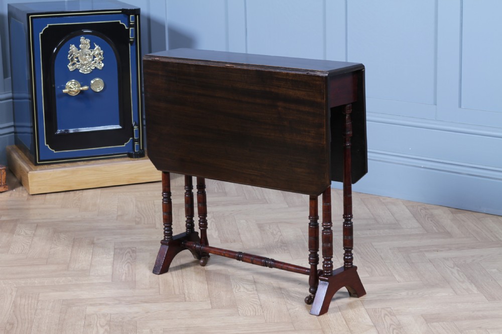 An Edwardian solid mahogany Sutherland table with folded drop-leaf sides, turned spindle legs, and ceramic castors on trestle feet. View II