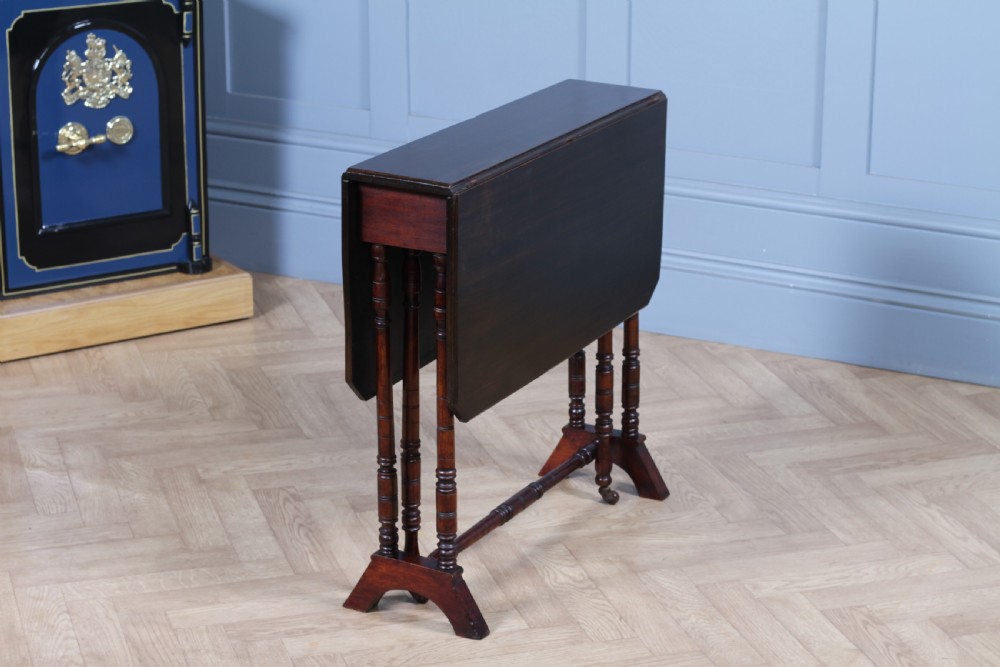 An Edwardian solid mahogany Sutherland table with folded drop-leaf sides, turned spindle legs, and ceramic castors on trestle feet. View III