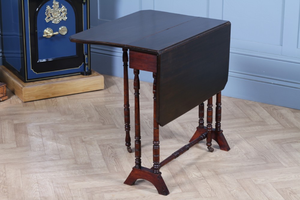 An Edwardian solid mahogany Sutherland table with folded drop-leaf sides, turned spindle legs, and ceramic castors on trestle feet. View V