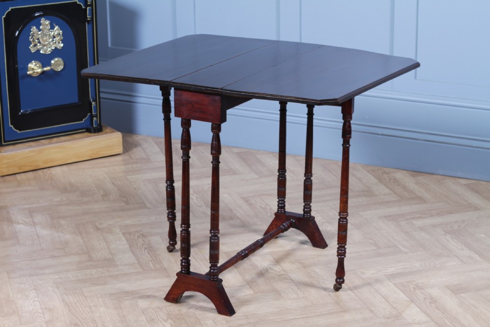 An Edwardian solid mahogany Sutherland table with folded drop-leaf sides, turned spindle legs, and ceramic castors on trestle feet. View VI
