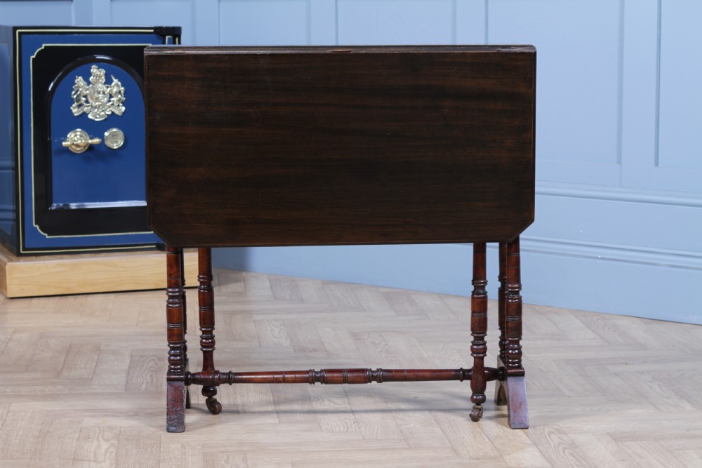 An Edwardian solid mahogany Sutherland table with folded drop-leaf sides, turned spindle legs, and ceramic castors on trestle feet. View VII