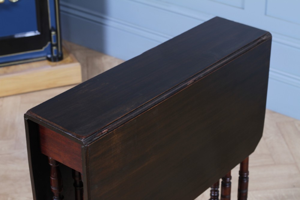 An Edwardian solid mahogany Sutherland table with folded drop-leaf sides, turned spindle legs, and ceramic castors on trestle feet. View VIII