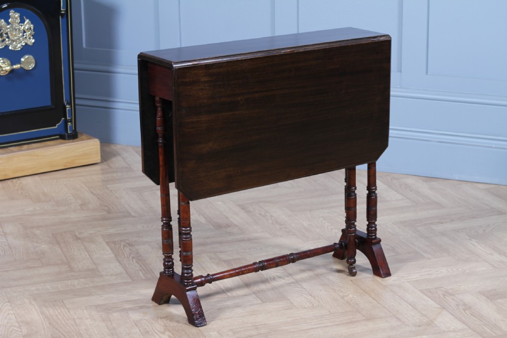 An Edwardian solid mahogany Sutherland table with folded drop-leaf sides, turned spindle legs, and ceramic castors on trestle feet. View X