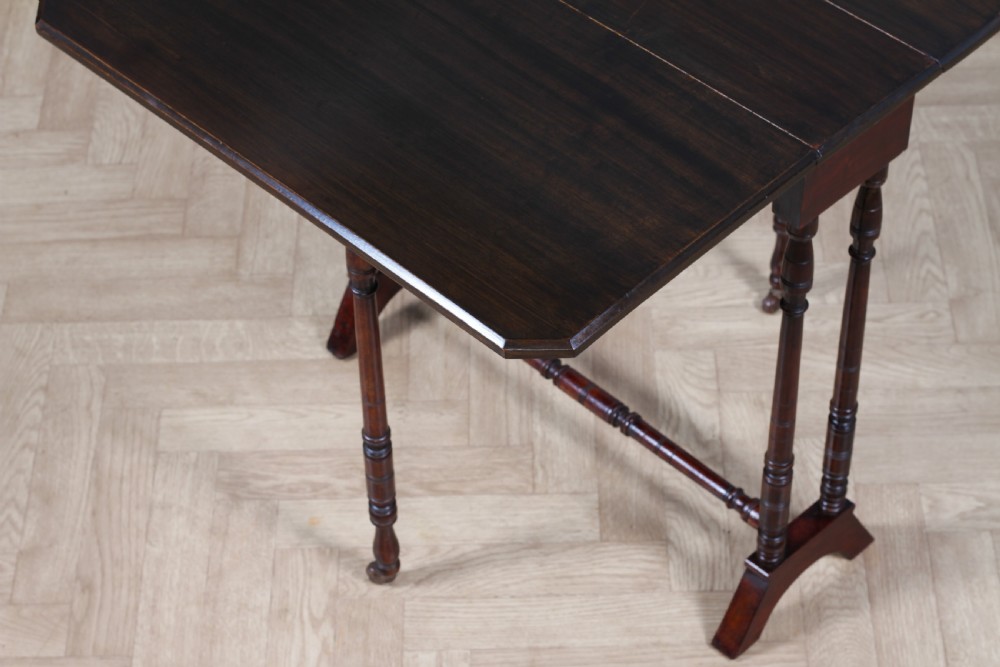An Edwardian solid mahogany Sutherland table with folded drop-leaf sides, turned spindle legs, and ceramic castors on trestle feet. View XI
