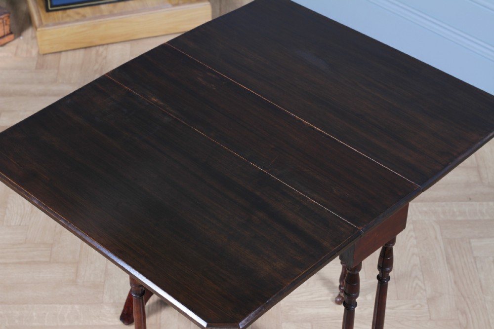 An Edwardian solid mahogany Sutherland table with folded drop-leaf sides, turned spindle legs, and ceramic castors on trestle feet. View XII