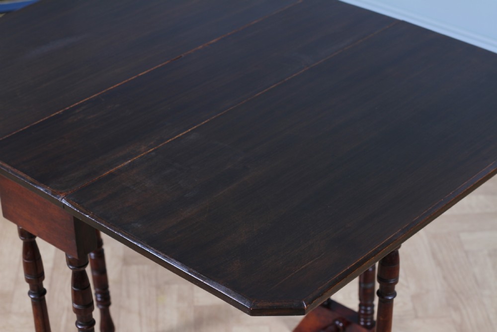 An Edwardian solid mahogany Sutherland table with folded drop-leaf sides, turned spindle legs, and ceramic castors on trestle feet. View XV