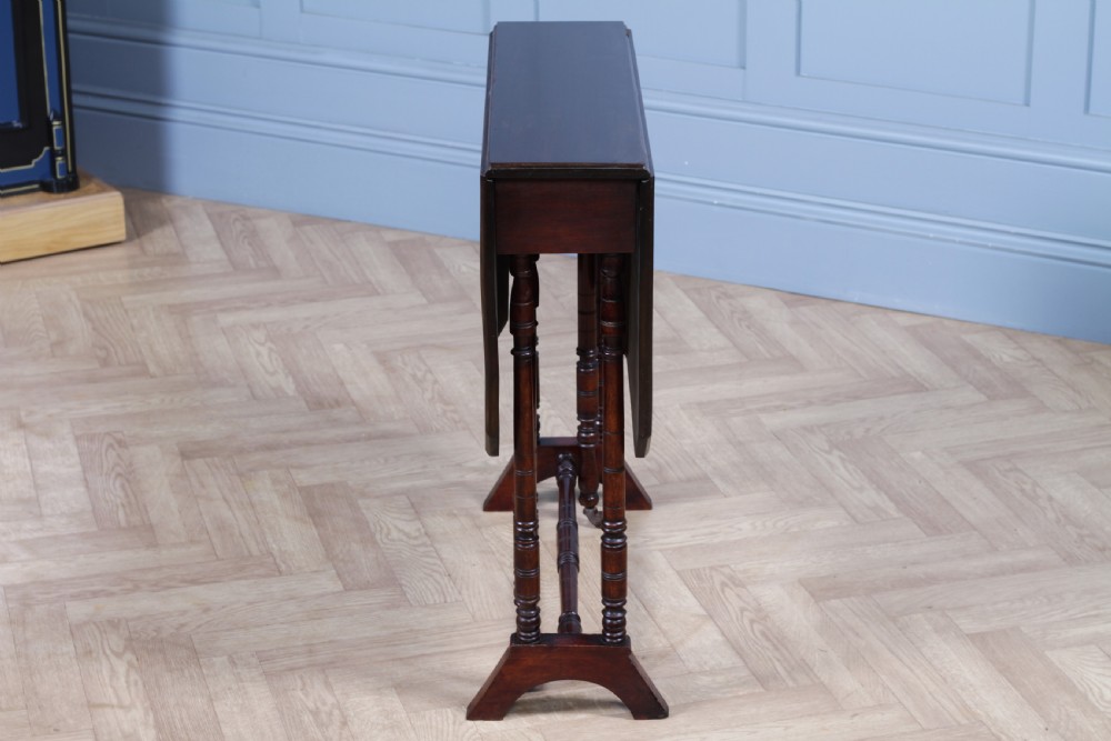 An Edwardian solid mahogany Sutherland table with folded drop-leaf sides, turned spindle legs, and ceramic castors on trestle feet. View XVI