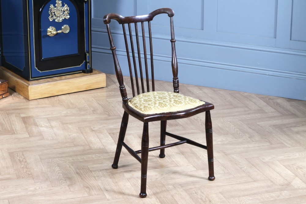 An Edwardian dark walnut nursing chair featuring a spindled stick back, turned legs, and a patterned yellow fabric seat.