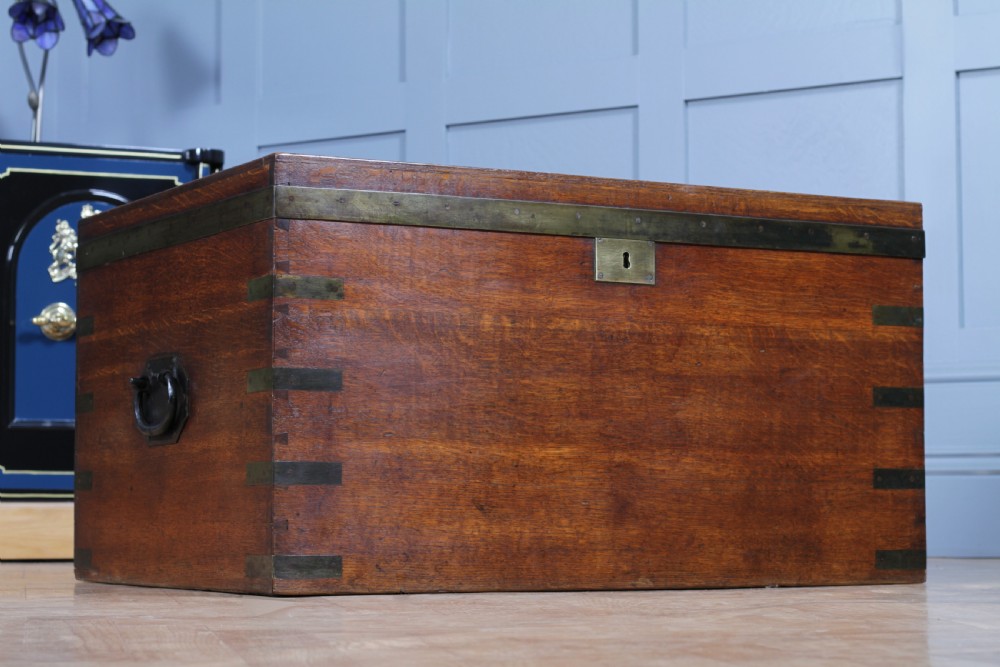 An open Victorian oak campaign trunk featuring brass-bound corners, a central brass keyhole escutcheon, and a fitted interior lined in deep red velvet. View IV