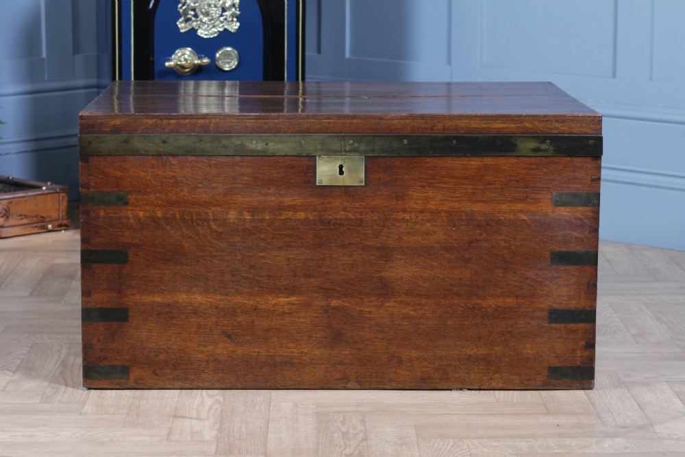 An open Victorian oak campaign trunk featuring brass-bound corners, a central brass keyhole escutcheon, and a fitted interior lined in deep red velvet. View V