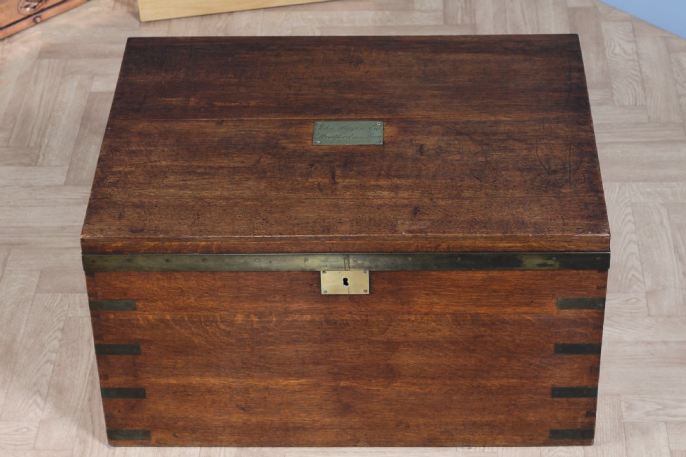 An open Victorian oak campaign trunk featuring brass-bound corners, a central brass keyhole escutcheon, and a fitted interior lined in deep red velvet. View VI