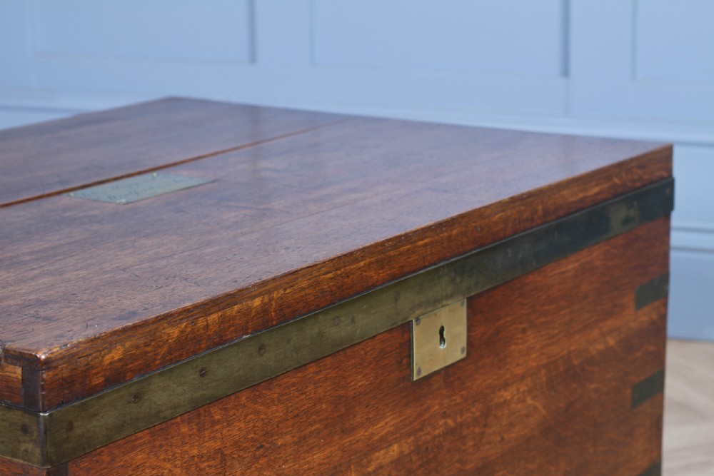 An open Victorian oak campaign trunk featuring brass-bound corners, a central brass keyhole escutcheon, and a fitted interior lined in deep red velvet. View X
