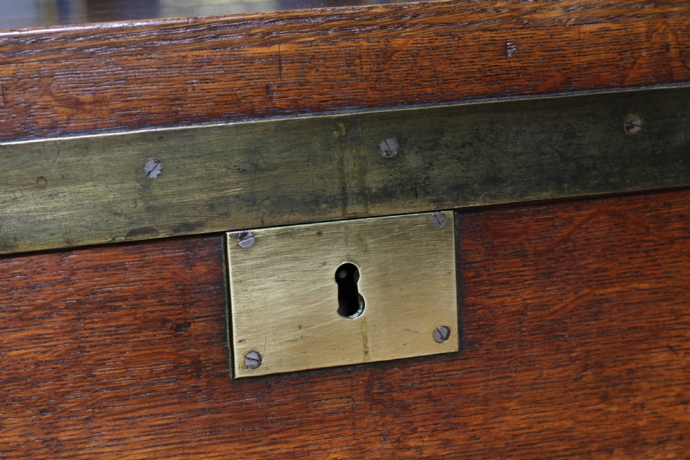 An open Victorian oak campaign trunk featuring brass-bound corners, a central brass keyhole escutcheon, and a fitted interior lined in deep red velvet. View XIII
