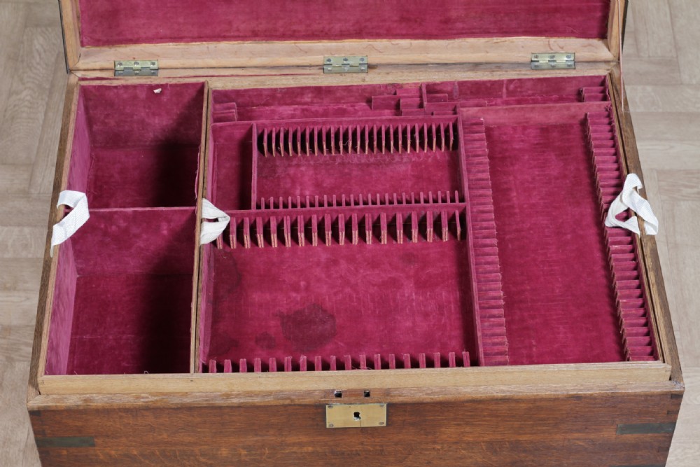 An open Victorian oak campaign trunk featuring brass-bound corners, a central brass keyhole escutcheon, and a fitted interior lined in deep red velvet. View XVIII