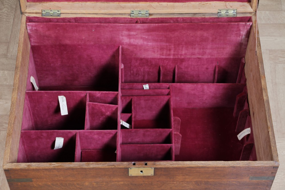 An open Victorian oak campaign trunk featuring brass-bound corners, a central brass keyhole escutcheon, and a fitted interior lined in deep red velvet. View XIX