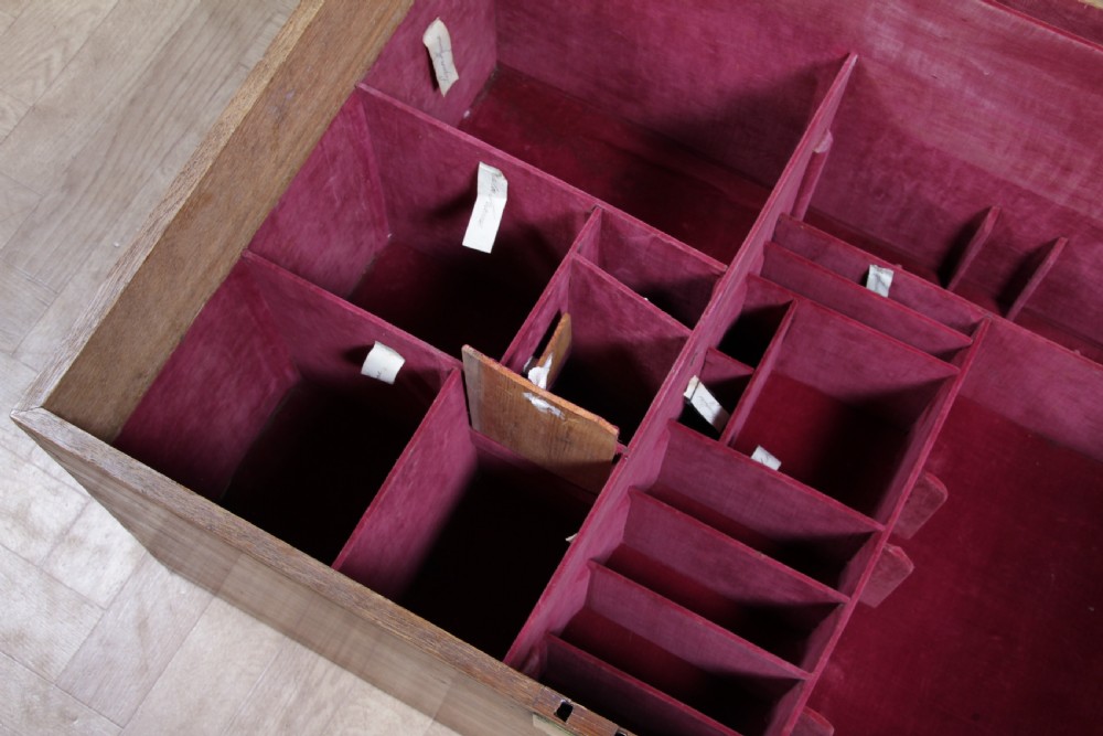 An open Victorian oak campaign trunk featuring brass-bound corners, a central brass keyhole escutcheon, and a fitted interior lined in deep red velvet. View XXI