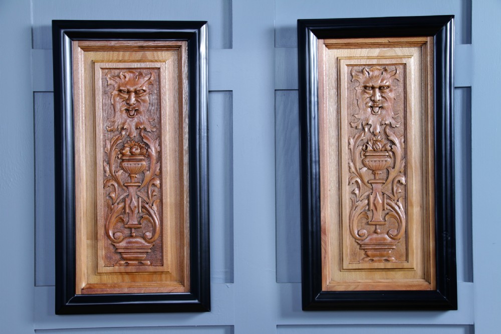 A pair of rectangular carved walnut wall panels featuring detailed grotesque masks and classical urns set within black ebonised frames. View II