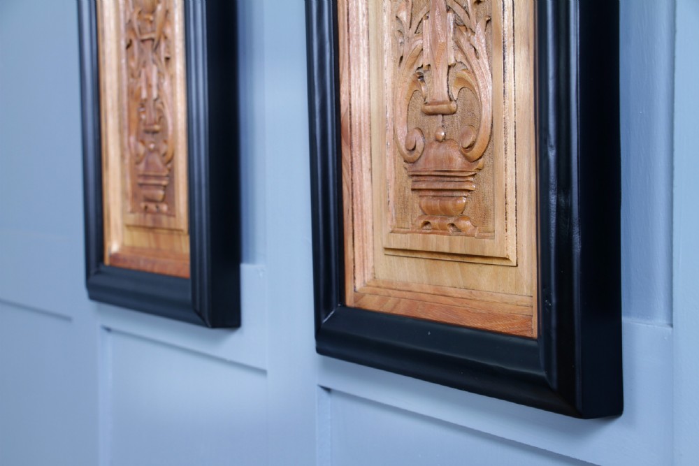 A pair of rectangular carved walnut wall panels featuring detailed grotesque masks and classical urns set within black ebonised frames. View V