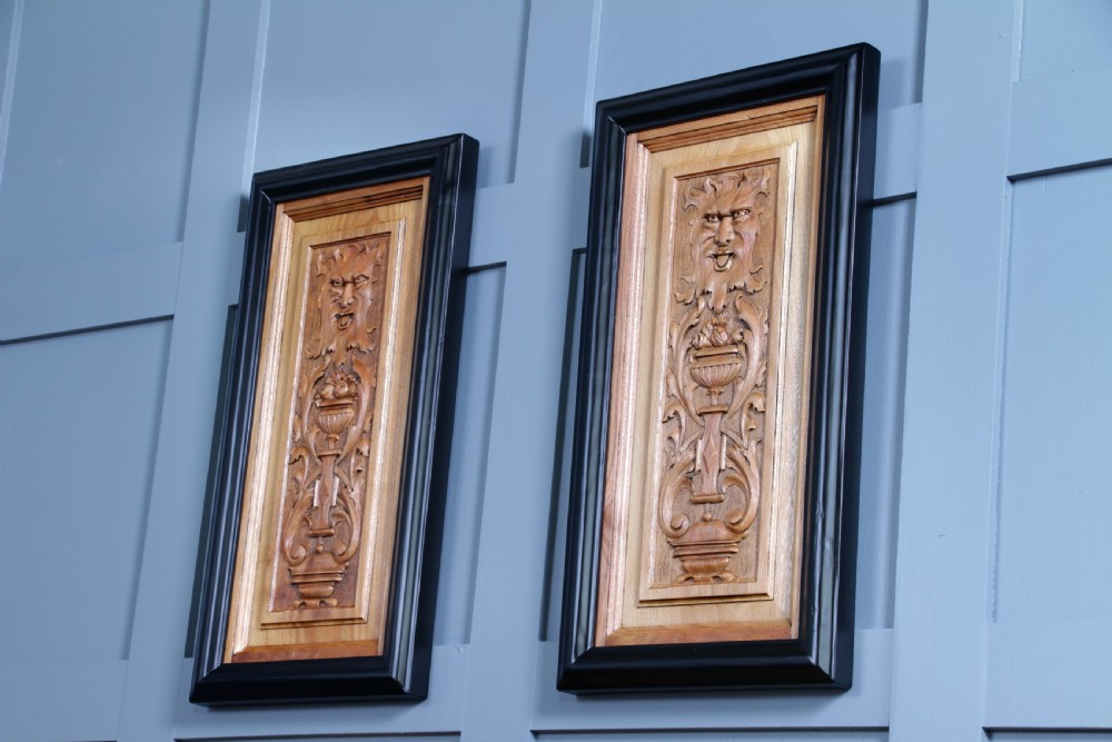 A pair of rectangular carved walnut wall panels featuring detailed grotesque masks and classical urns set within black ebonised frames. View VI
