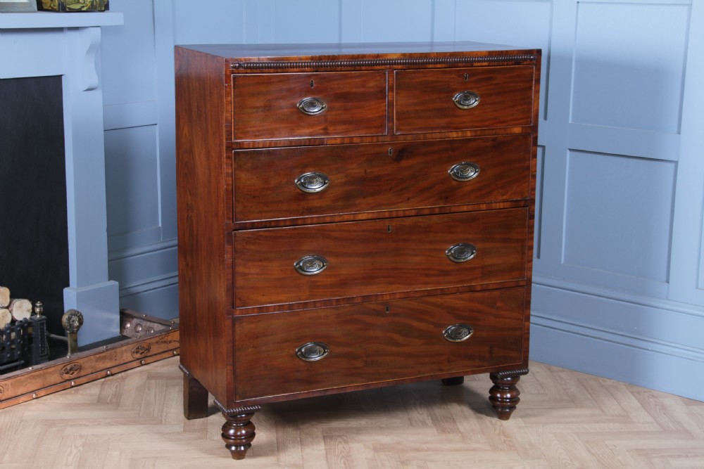 A William IV mahogany chest of drawers featuring two short over three long drawers with oval brass handles and turned feet.