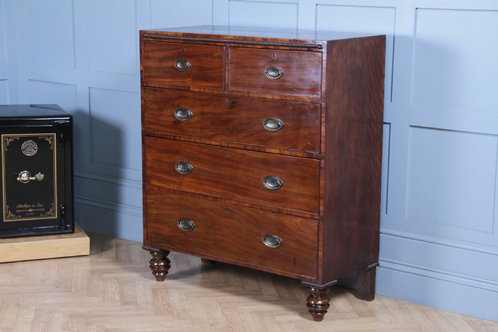 A William IV mahogany chest of drawers featuring two short over three long drawers with oval brass handles and turned feet. View III