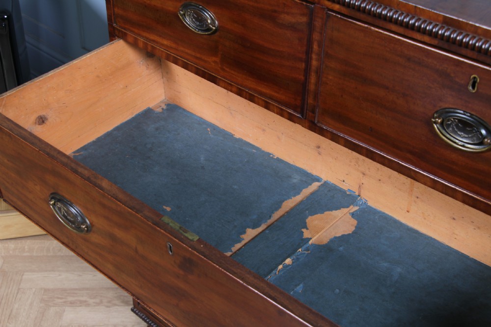 A William IV mahogany chest of drawers featuring two short over three long drawers with oval brass handles and turned feet. View VIII