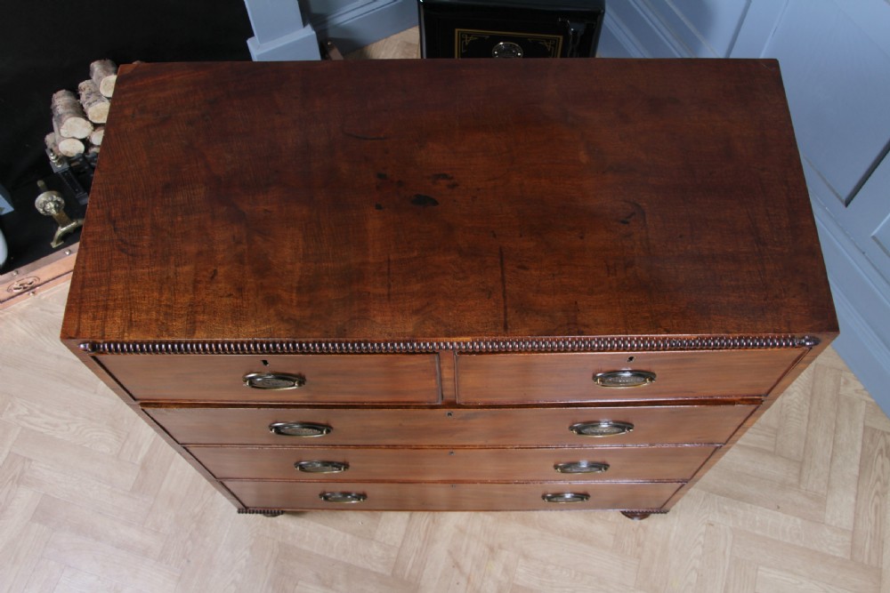 A William IV mahogany chest of drawers featuring two short over three long drawers with oval brass handles and turned feet. View IX