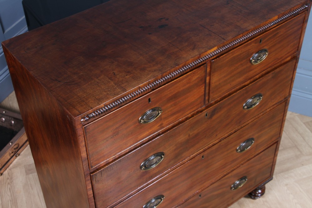 A William IV mahogany chest of drawers featuring two short over three long drawers with oval brass handles and turned feet. View XI