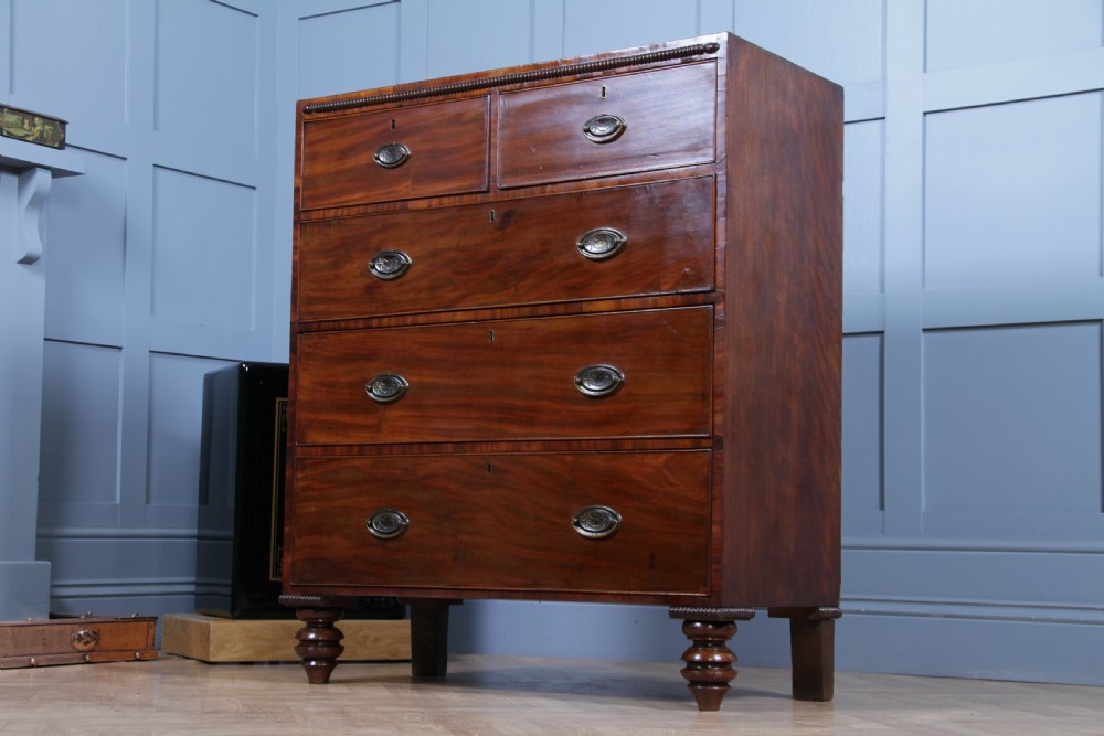 A William IV mahogany chest of drawers featuring two short over three long drawers with oval brass handles and turned feet. View XIII