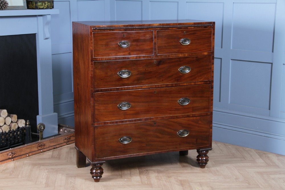 A William IV mahogany chest of drawers featuring two short over three long drawers with oval brass handles and turned feet. View XIV