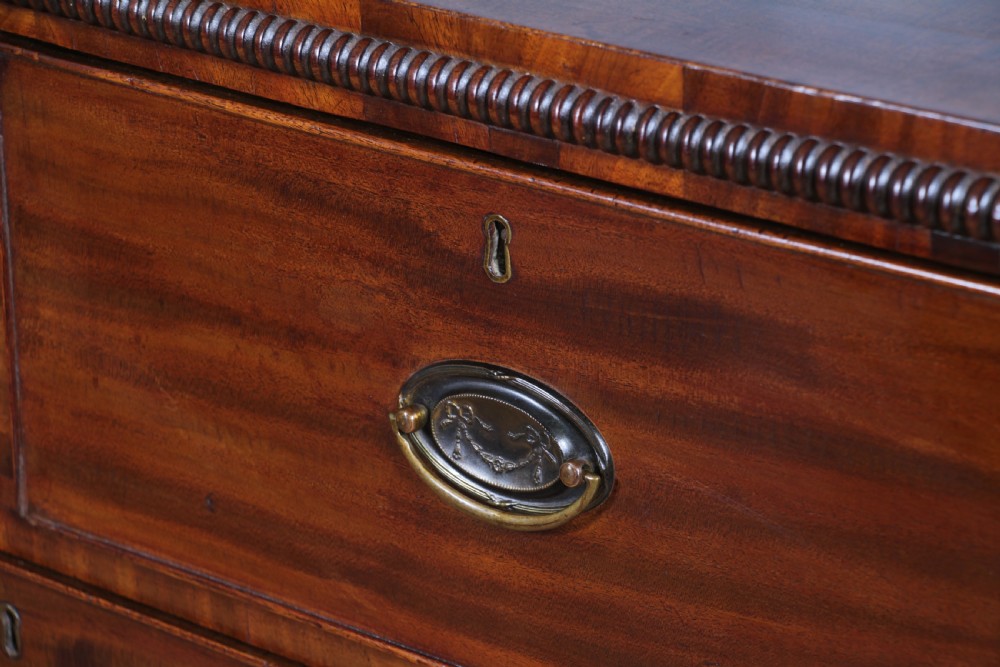A William IV mahogany chest of drawers featuring two short over three long drawers with oval brass handles and turned feet. View XVI