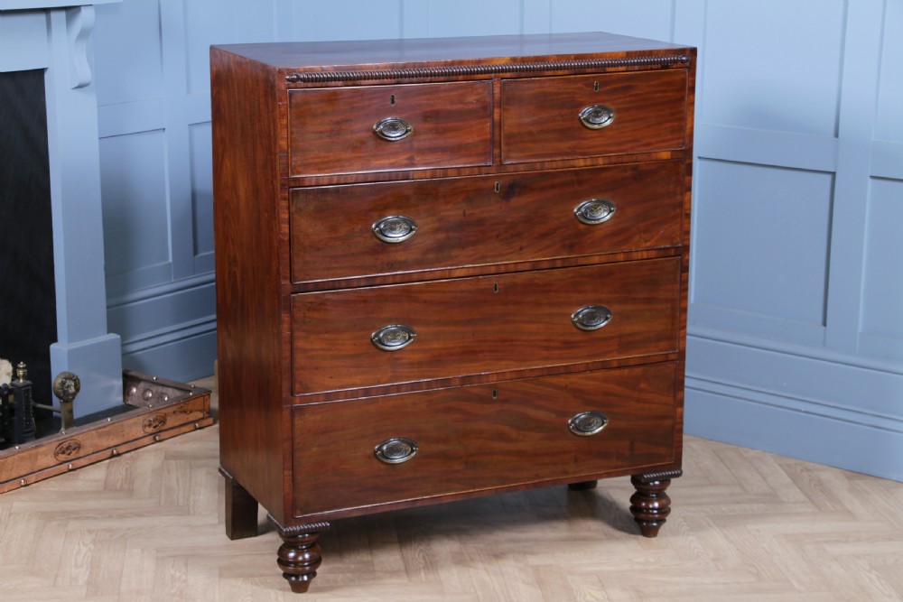 A William IV mahogany chest of drawers featuring two short over three long drawers with oval brass handles and turned feet. View XVII