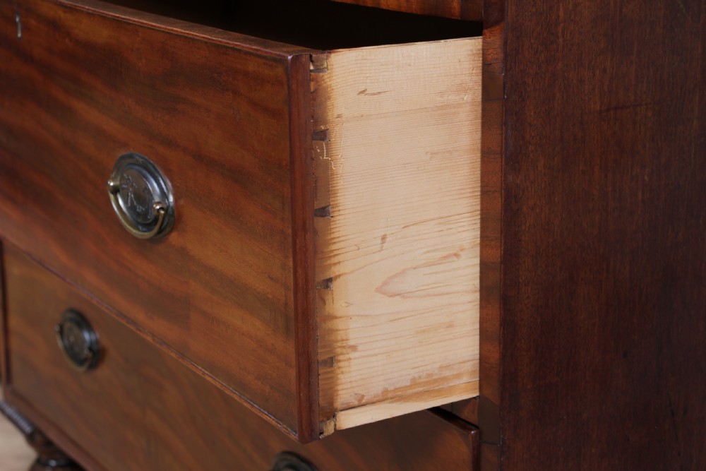 A William IV mahogany chest of drawers featuring two short over three long drawers with oval brass handles and turned feet. View XIX