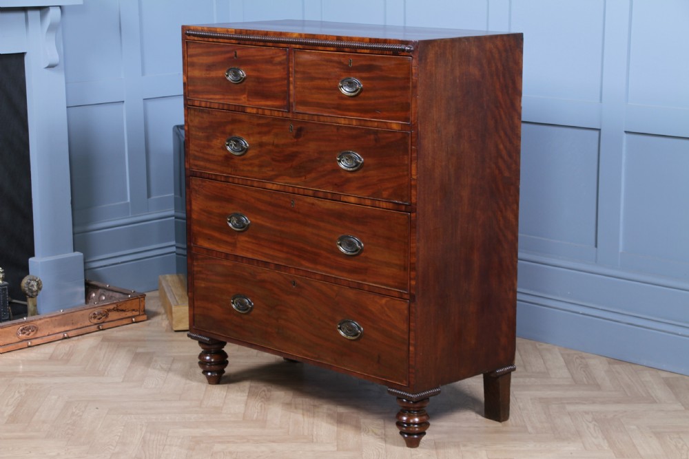 A William IV mahogany chest of drawers featuring two short over three long drawers with oval brass handles and turned feet. View XX