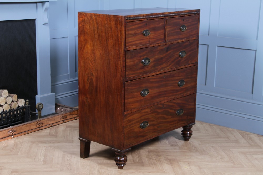 A William IV mahogany chest of drawers featuring two short over three long drawers with oval brass handles and turned feet. View XXI